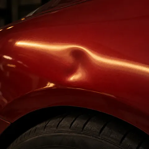 Illustration — bosse creusée dans l’aile rouge d’une voiture, au-dessus de la roue.