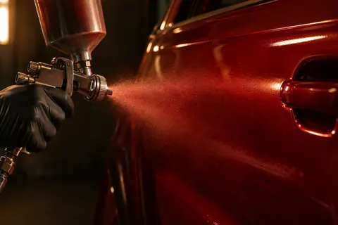 Illustration — pistolet de peinture en action sur une portière rouge, brouillard de peinture en cabine.